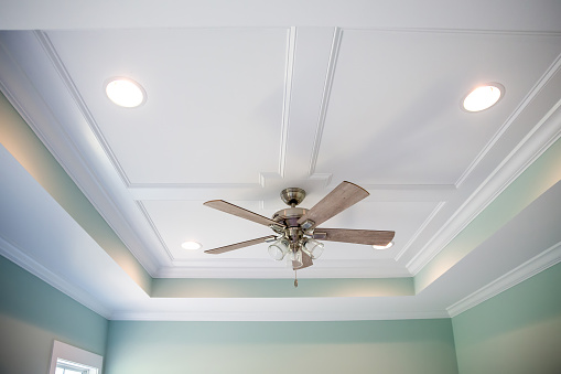 White tray ceiling in small new construction house with windows and a ceiling fan