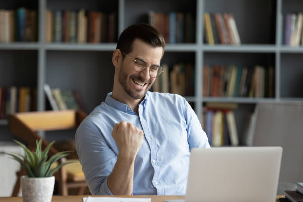 Excited man celebrating success, reading good news in email Excited man wearing glasses celebrating success, reading good news in email, happy overjoyed businessman looking at laptop screen, showing yes gesture and laughing, sitting at work desk sales win stock pictures, royalty-free photos & images