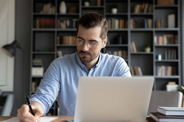 istock Confident businessman writing notes, sitting at work desk with laptop 1223044291