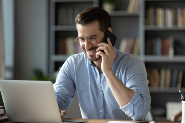 istock Smiling businessman talking on phone, looking at laptop screen 1223044298