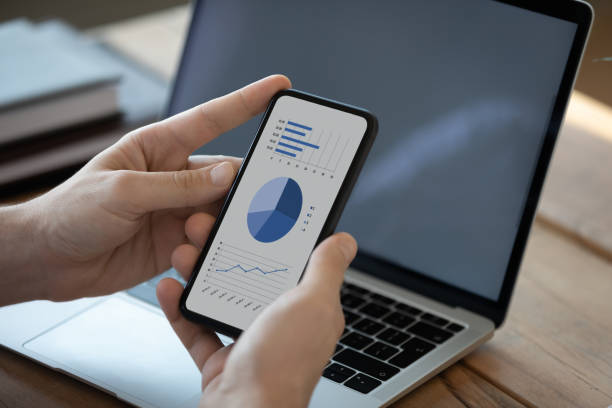 istock Close up businessman holding phone with diagrams on screen 1223044327