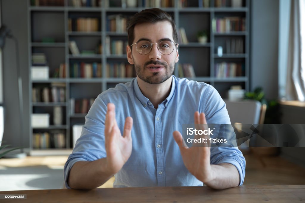 Head shot confident businessman coach looking at camera and talking Head shot portrait confident businessman coach wearing glasses looking at camera and talking, mentor speaker holding online lesson, explaining, sitting at wooden work desk in modern cabinet Talking Stock Photo