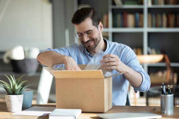 istock Smiling man unpacking awaited parcel, sitting at work desk 1223044362