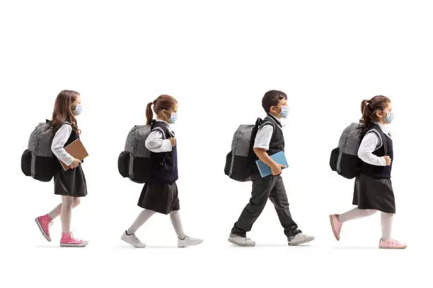 Photo of Schoolchildren in uniforms walking in line and wearing protective face masks