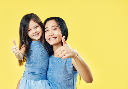 Happy mother and her child daughter showing thumbs up and have fun together on yellow background. Family,  motivation concept