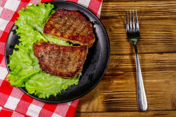 istock Grilled pork steaks with lettuce leaves on wooden table. Top view 1223050761