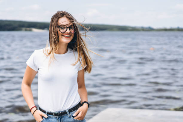 Portrait of a beautiful young woman in stylish glasses. Girl in white tshirt posing on the background of the lake landscape stock photo