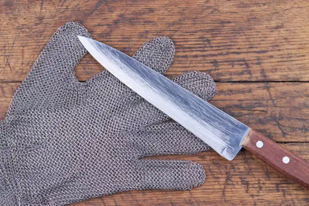 View from above for chain mail glove with kitchen knife. wooden board background.
