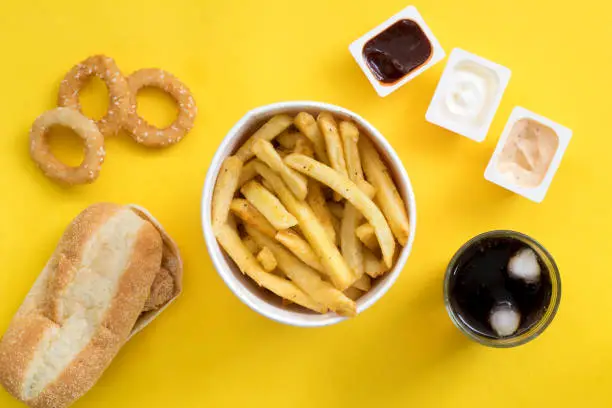 Photo of Fast food dish top view. Chicken burger, potato chips and wedges. Take away composition. French fries, hamburger, mayonnaise and ketchup sauces on yellow background.