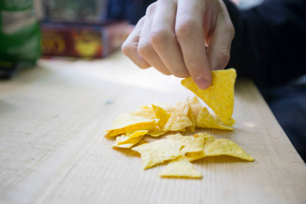 close-up of young man eating chips from wooden table - tortilla chip imagens e fotografias de stock