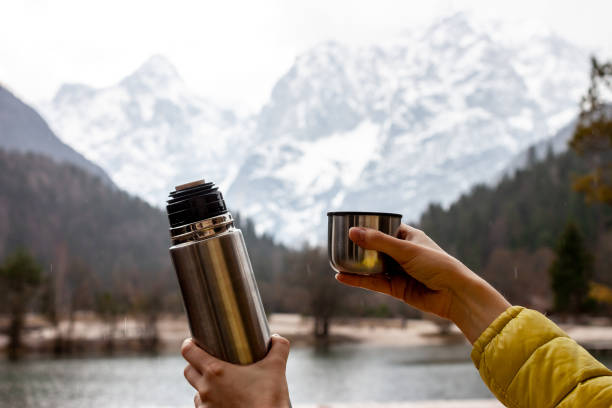 istock female hands keep thermos and cup in front of lake 1223057057