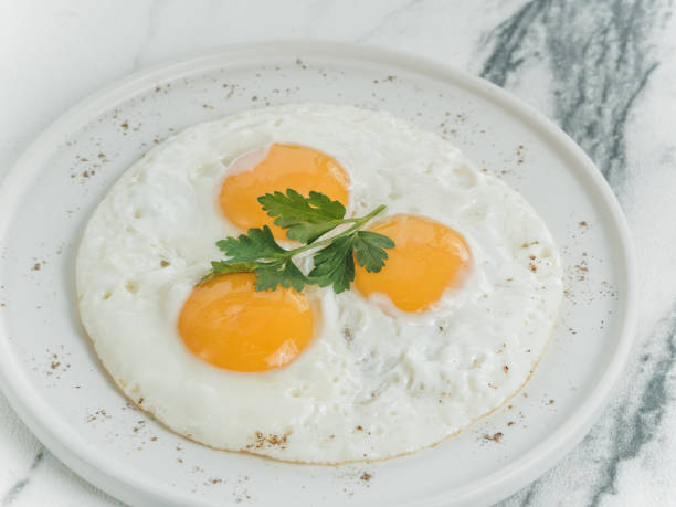 istock Breakfast is three eggs fried on a white plate on a white marble background. Decorated with parsley. Scrambled eggs with cheese. Photo for the menu. 1223057159
