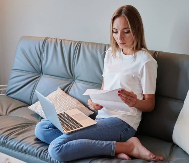 istock Young female with laptop on the couch reading eviction letter 1223059076