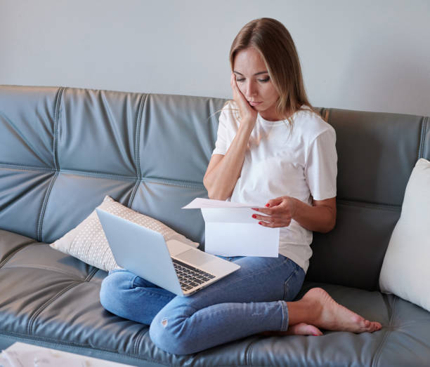 istock Young female with laptop on the couch reading eviction letter 1223059397