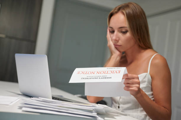 Worried young female with laptop reading eviction letter at home stock photo