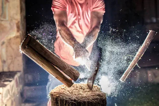 A man chops a piece of firewood. In the same moment as the wood splits the photograph is taken with a backlit flash. Freezing all the small particles that explodes.