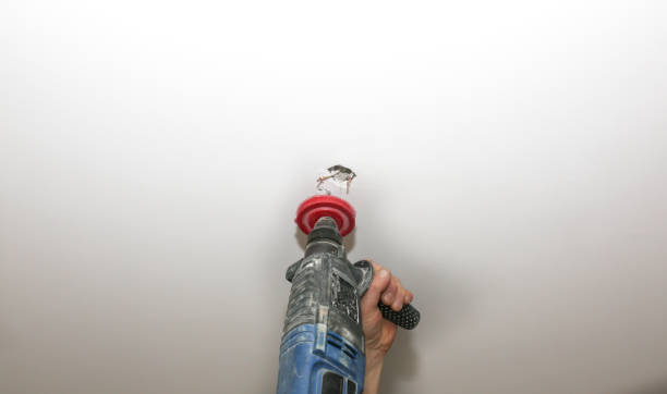 istock Lamp installation. Man making hole in the ceiling with electric drill. Restoration indoors. Maintenance work. 1223061035