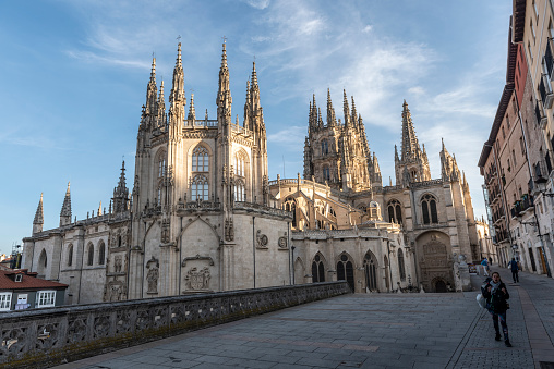 A pilgrim walking the Camino de Santiago carries her backpack on a street outside Burgos Cathedral, a Gothic church that also includes decorative Renaissance and Baroque elements, in Burgos, Spain. It is a UNESCO World Heritage Site. (June 13, 2018)