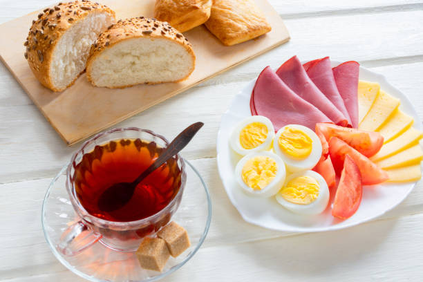 Fresh delicious breakfast with soft boiled egg, cheese, ham fresh bread and cup coffee or tea on light wooden background. Healty contenintal breakfast.