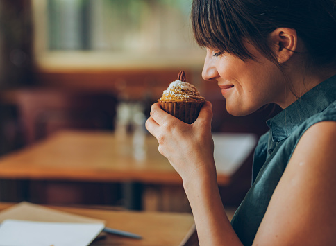 Smiling woman smelling a delicious orange cupcake she's about to taste at her favourite cafe.