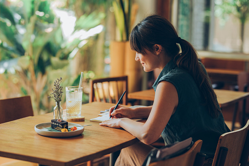 Happy Young Woman Writing Notes in her Notebook while Sitting at a Cafe photo