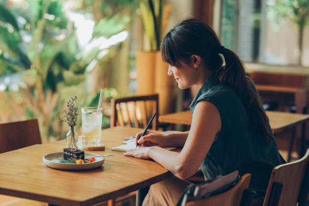 Happy Young Woman Writing Notes in her Notebook while Sitting at a Cafe