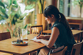 Happy Young Woman Writing Notes in her Notebook while Sitting at a Cafe