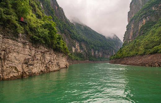 Wuchan, China - May 7, 2010: Dawu or Misty Gorge on Daning River. Bend in canyon with brown rocky cliffs, green foliage on top, emerald green water, and misty cloudscape.