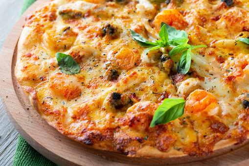 Seafood thin tasty pizza with shrimps, mussels and basil on wooden background, close-up
