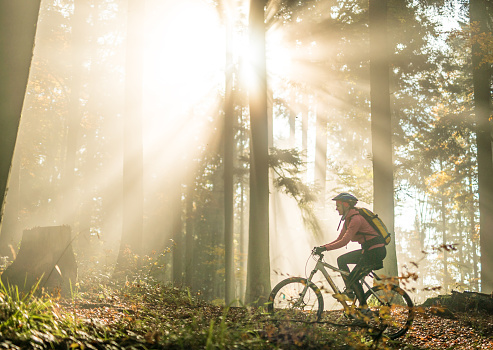 Young woman rides bike through forest at sunrise