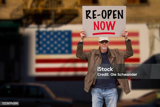 Protester With Cap And Sunglasses Demonstrate Against Stayathome Orders Due To The Covid19 Pandemic With Sign Saying Reopen Big American Flag On Background Stock Photo - Download Image Now