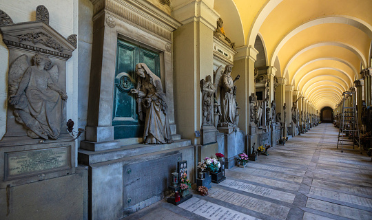 Milan, Italy - May 17, 2017: White marble sculptures on the tombs are covered with dust and cobwebs. Monumental Cemetery of Staglieno is a crisscrossing of large ancient burial niches arcades located on a hillside in the district of Staglieno of Genoa, Italy.