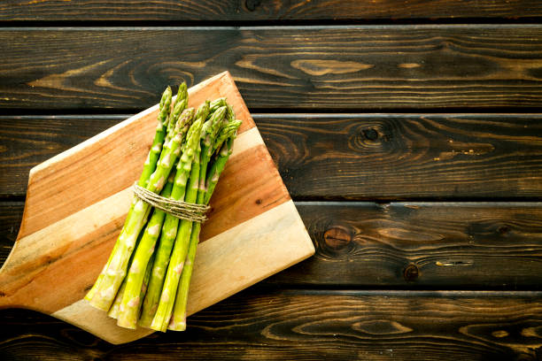 istock Cooking asparagus. Bunch steams on cutting board on dark wooden background top-down copy space 1223078431