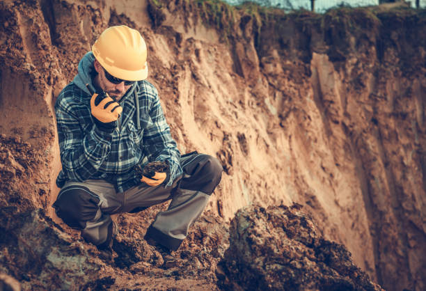 Caucasian Male Engineering Geologist Talking On Radio At Construction Site. Construction Geologist Assessing Job Site And Communitacing With Workers Through Walkie Talkie. geologist stock pictures, royalty-free photos & images