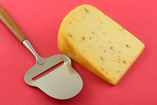 Spicy hot pepper gouda cheese with jalapeno, chipotle and habanero peppers and cheese slicer on red background