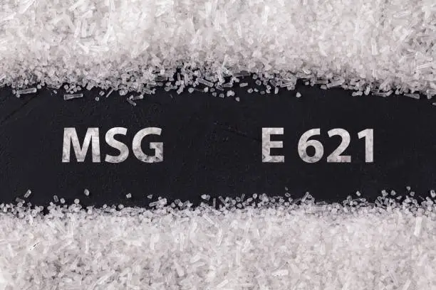 Closeup texture Monosodium glutamate on dark background with text MSG  E621 . Sodium salt used as flavor enhancer. Food ingredient.