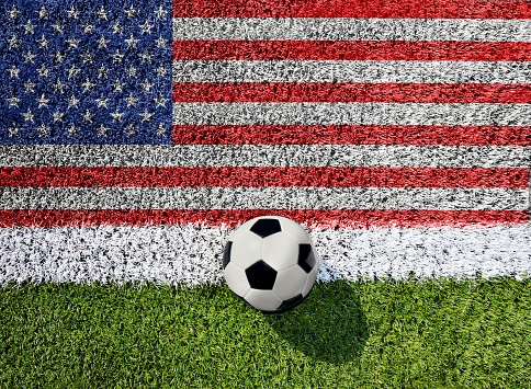 Soccer or football on green grass, on flag of United States of America background