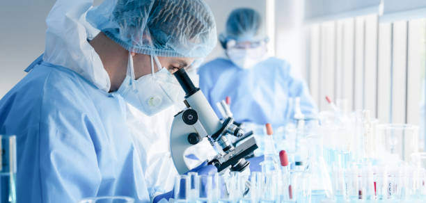 biochemical research scientist team working with microscope for coronavirus vaccine development in pharmaceutical research labolatory stock photo