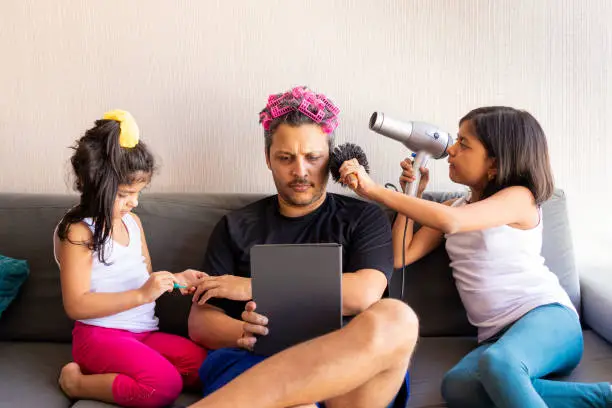 Pretty daughters are painting the nails and combing the hair of their handsome young father