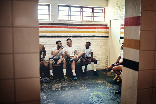 Full length shot of a group of handsome young rugby players having a chat while sitting together in a locker room