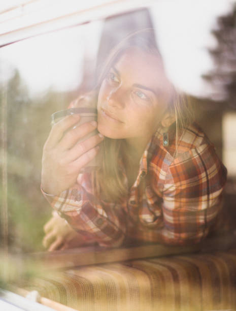jeune femme regardant avec impatience hors de sa fenêtre - longingly photos et images de collection