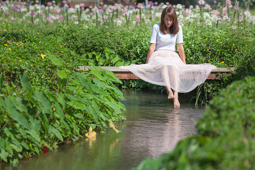 Asian woman relaxing on little wooden bridge over the rivulet in flower garden, Relaxation concept, Daydream or imagine in the nature background