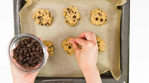 Photo of Chocolate Chip Cookies recipe. Woman placing chocolate chips on the top of unbaked cookies, close up, view from above