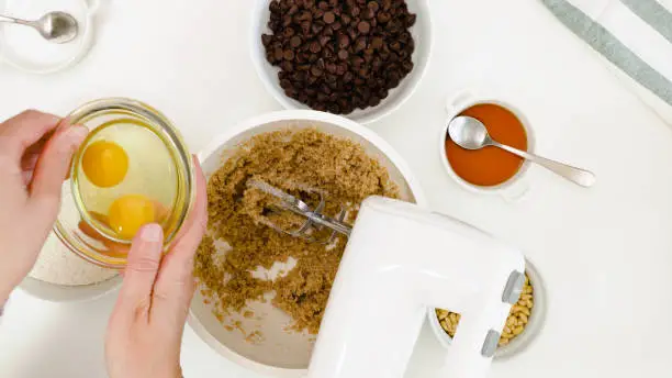 Photo of Chocolate Chip Cookies recipe. Chef placing eggs in a bowl, close up on white background, view from above