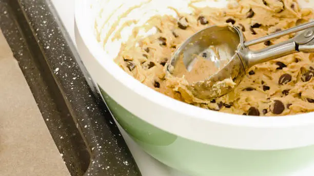 Photo of Chocolate Chip Cookie batter close up in a bowl on white kitchen table.