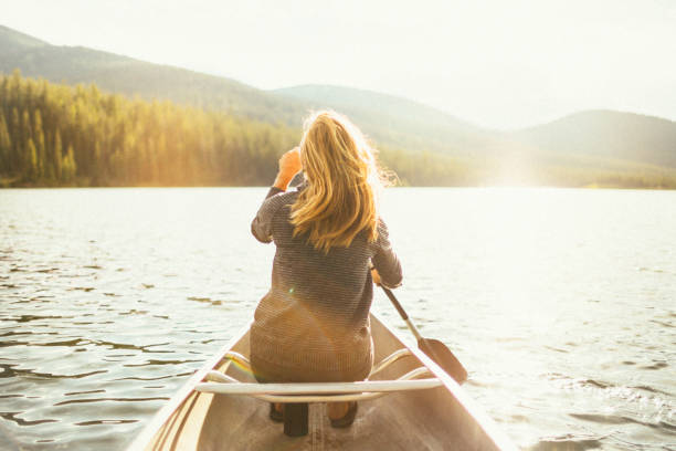 美しい健康なアクティブな女性は夕日に湖でカヌー - montana outdoor pursuit canoe canoeing ストックフォトと画像