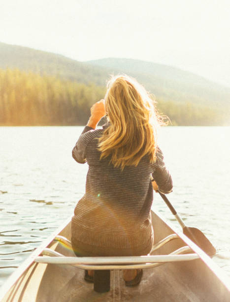 美しい健康なアクティブな女性は夕日に湖でカヌー - montana outdoor pursuit canoe canoeing ストックフォトと画像