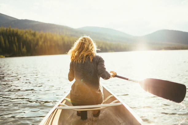 美しい健康なアクティブな女性は夕日に湖でカヌー - montana outdoor pursuit canoe canoeing ストックフォトと画像