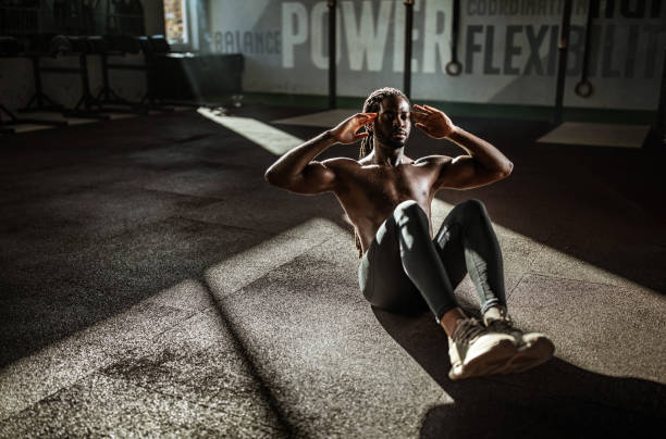 Sweaty black athlete doing sit-ups in a gym. African American male athlete exercising sit-ups with hands behind his head in a gym. Copy space. sit ups stock pictures, royalty-free photos & images