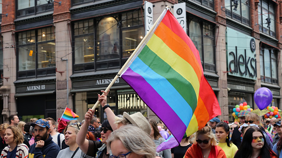 Helsinki Pride photographed in Helsinki, Finland, June 2019. People marching for equal rights for LGBT community with rainbow flags and colorful signs. Color image of the parade symboling equality. Big rainbow flags carrying by people in the parade. Photographed in Aleksanterinkatu, Helsinki.